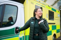 A uniformed ambulance worker with her hand on the ambulance door handle while looking in the opposite direction