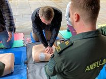 A member of the public performs CPR on a training manikin while a Community First Responder observes and provides guidance during a lifesaving skills demonstration
