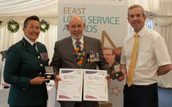 A man receives a long service award for 40 years from a paramedic in dress uniform and a CEO in a shirt and tie