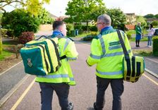 Two uniformed community first responders carrying equipment bags walking down a road