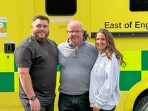 Three individuals standing in front of a stationery ambulance