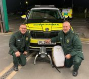 Two uniformed paramedics with a life-saving CPR device in front of a rapid response car