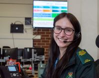 Female call handler in headset smiling at the camera, sitting in the control room