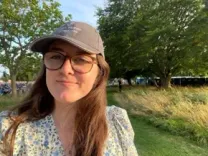 A woman wearing glasses and a hat surrounded by greenery