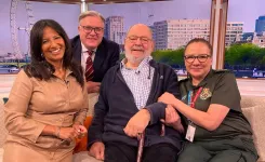 three people sitting on a studio couch and one person standing behind the couch, all smiling