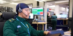 Someone in green uniform wearing a headset in an ambulance 999 call centre.
