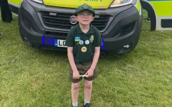 Isaac Hawes wearing his scouts uniform and standing in front of a stationary ambulance