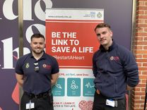 Two men from the Fire and Rescue Service stand in front of a pull-up banner promoting CPR