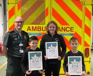 An uniformed paramedic with three children who are holding up framed bravery award certificates