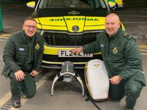 Two EEAST staff kneeling in front of an ambulance with a lucas device