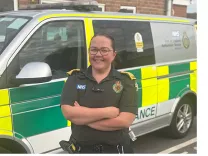 Paramedic Megan Kelly in uniform, standing in front of an ambulance response van