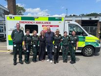 Grateful patient Paul Mann stands in front of an ambulance with his partner, Jo, and EEAST team Derek Wright, Jennifer Roberts, Evie Andrews, Abbie Wheeler, Kate Bennett and Justine Di Fede. Paul is pictured in the centre, with the group arranged alongside him for a photograph.
