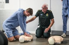 one man assists another as they practice cpr on a dummy