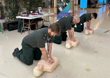 Three men in green ambulance uniform perform CPR on manikins