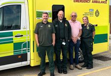 Three uniformed ambulance workers - two men and one woman - with a grateful patient in front of an ambulance