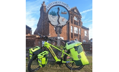 An electric bike stood upright by a kickstand in front of a sign for Wells-next-the-Sea