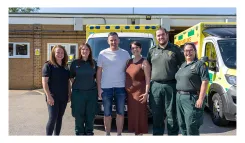 Tony Pearce stands with his wife, Claire, and four East of England Ambulance Service staff members in front of an ambulance following a reunion with the team who responded to his road traffic collision in March 2024.