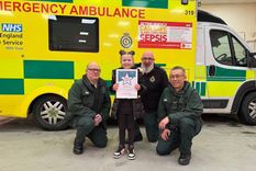 Three uniformed ambulance workers with a seven-year-old girl who is holding up a bravery award she has just been presented with 